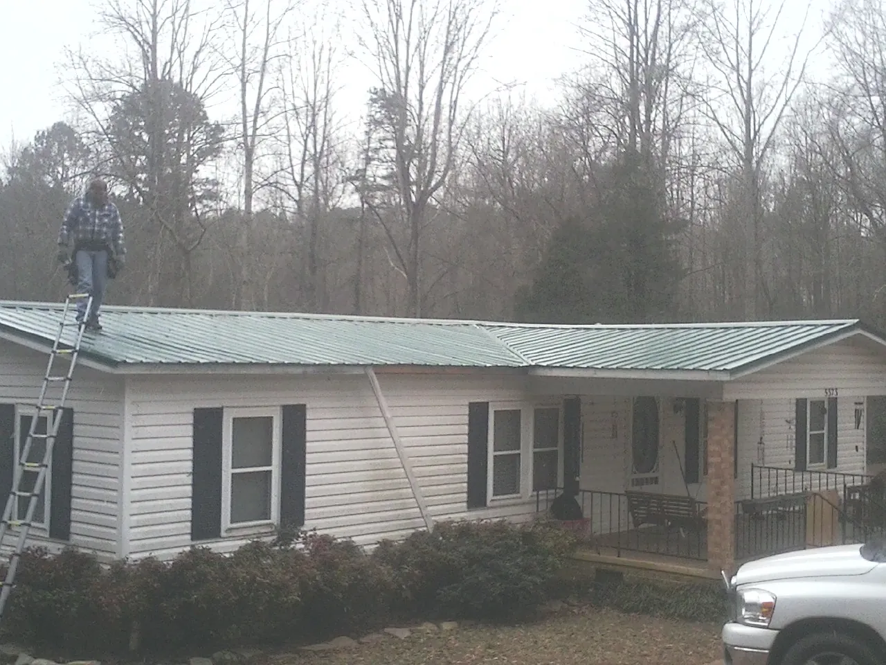 Worker on a ladder beside a new green metal roof on a ranch home in South Pomfret