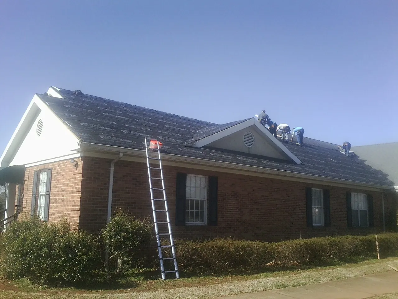 Crew tearing shingles off a brick ranch roof with a ladder set — Emergency Roof Repair work by our crew in South Pomfret