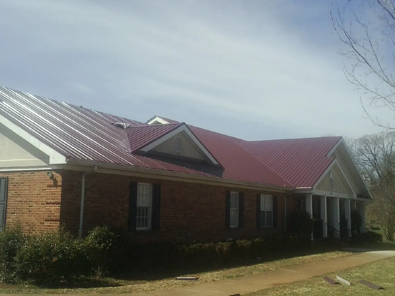 Red metal roof with gabled entries on a long brick building, from a Hail Damage Roof Repair job in South Pomfret