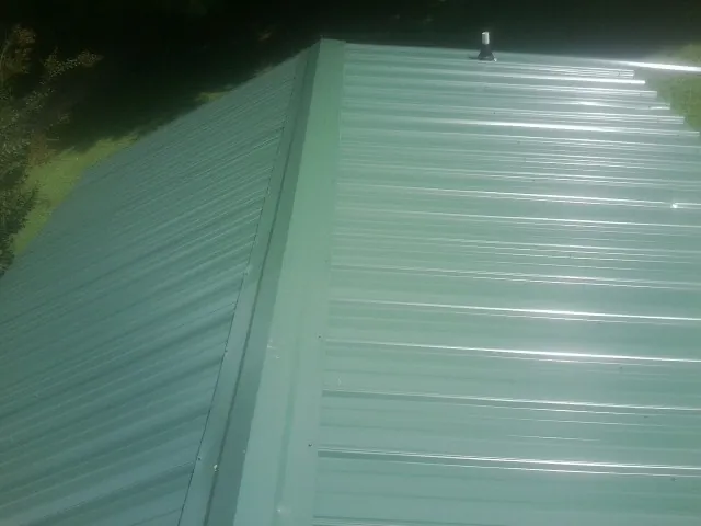 New green metal panels meeting at the ridge of a roof — Flat Roof Repair work by our crew in South Pomfret