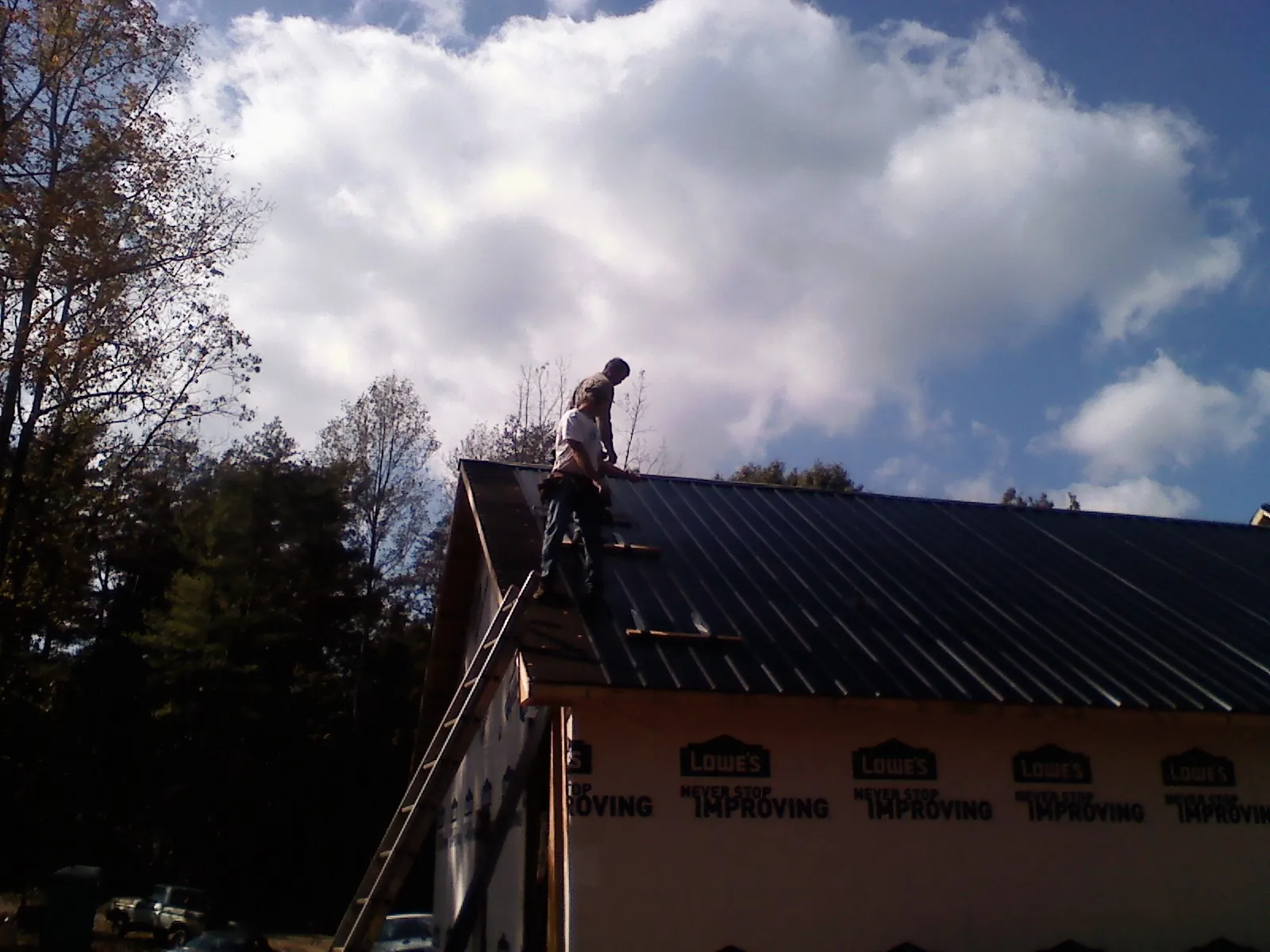 Roofer fastening dark metal panels high against a cloudy sky, from a Roof Inspection job in South Pomfret