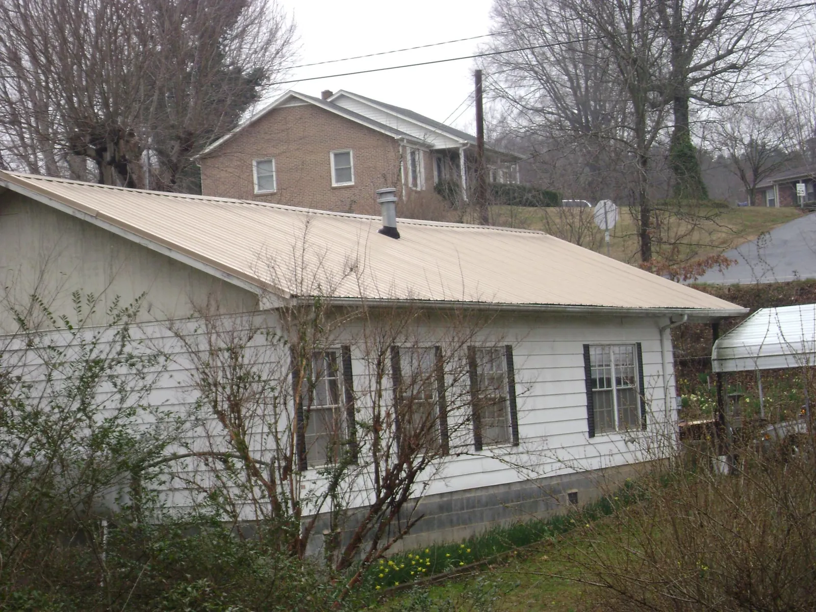 Tan metal roof on a white sided house set into a hillside — Commercial Roofing by Roofing Brothers in South Pomfret